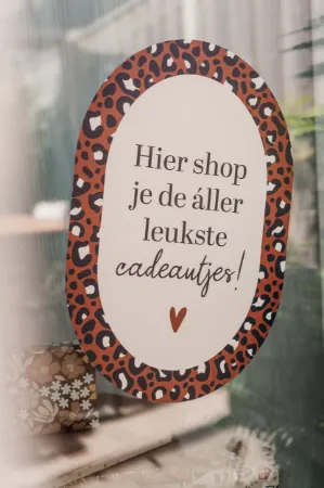 Sfeerbeeld raamsticker 40x60cm ovale vorm met mokka kleuren en panterprint rand, tekst "Hier shop je de allerleukste cadeautjes!" op een raam in de etalage
