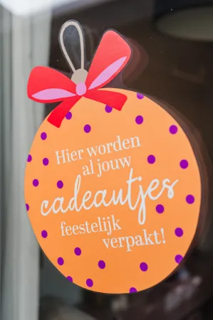 Raamsticker in de vorm van een kerstbal met vrolijke verpakkingstekst voor feestelijke etalages.